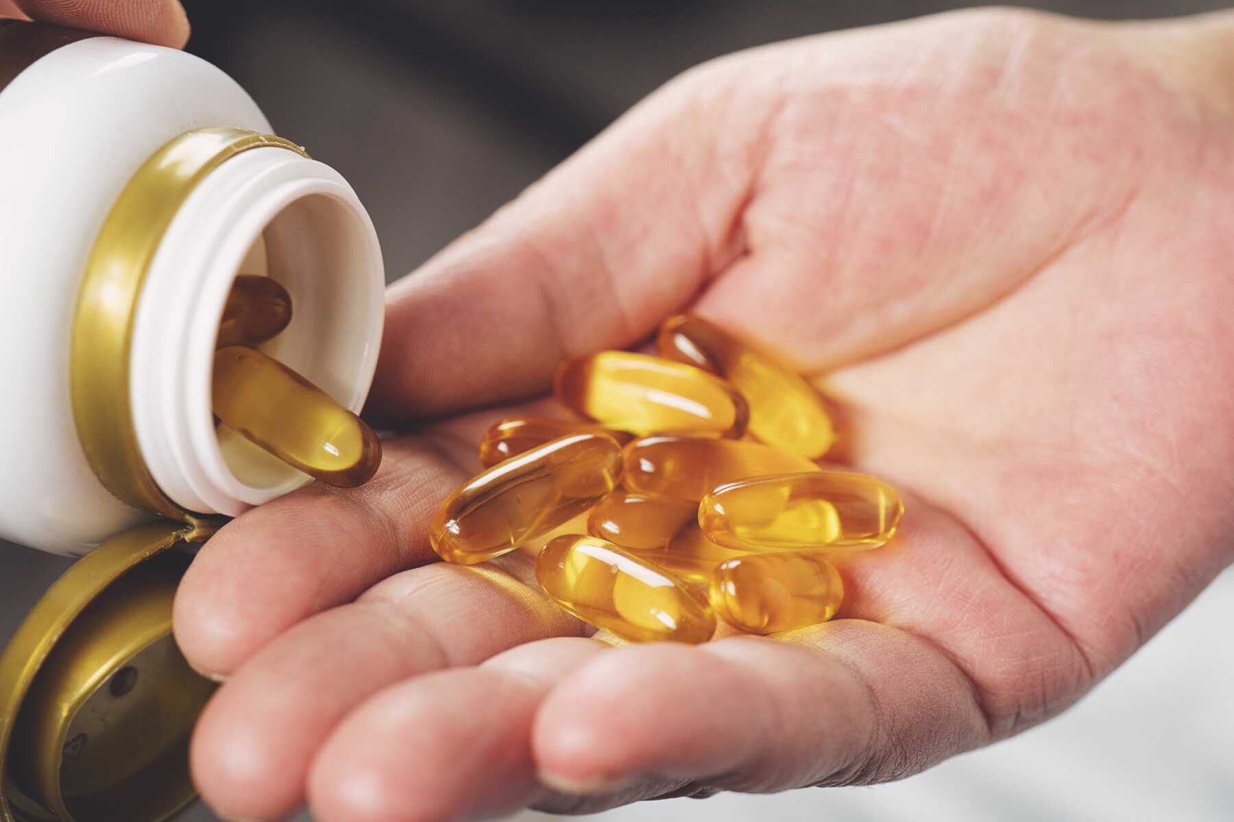 A hand holds gel capsules being dispensed from a pill bottle.