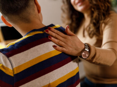 Close up shot of caring mother holding hand on her son's shoulder while assisting him homework and studying together.
