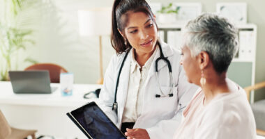 A doctor sporting a stethoscope around her neck shows a patient information on a tablet.