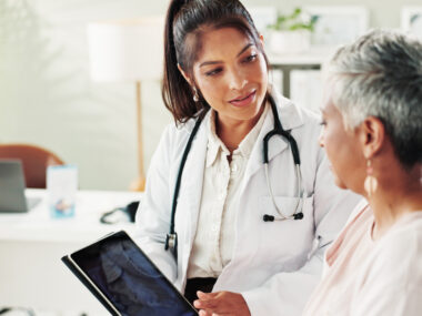 A doctor sporting a stethoscope around her neck shows a patient information on a tablet.