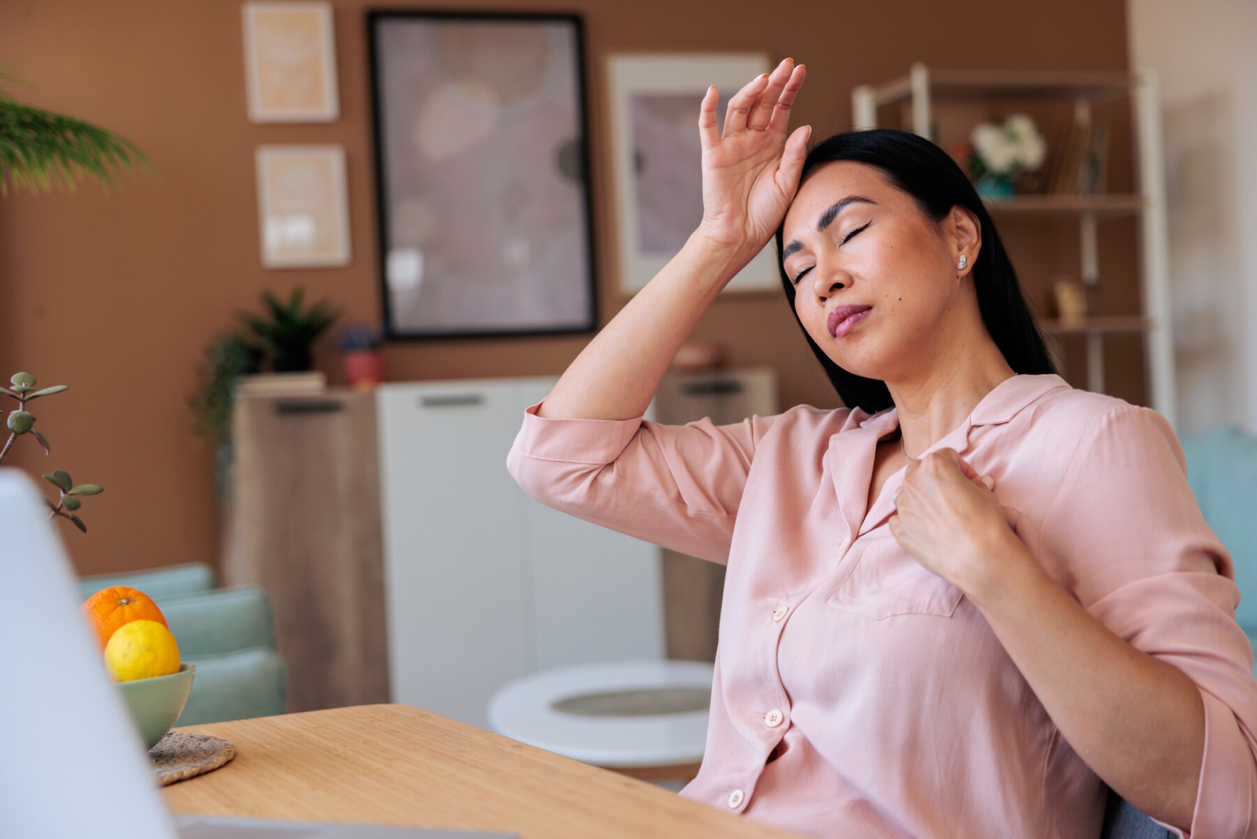 A woman experiencing a hot flash and headache during menopause holds her hand to her forehead while working on her laptop.