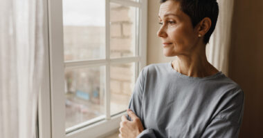 A woman with a pensive expression looks out a window.