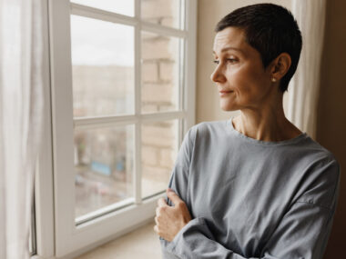 A woman with a pensive expression looks out a window.