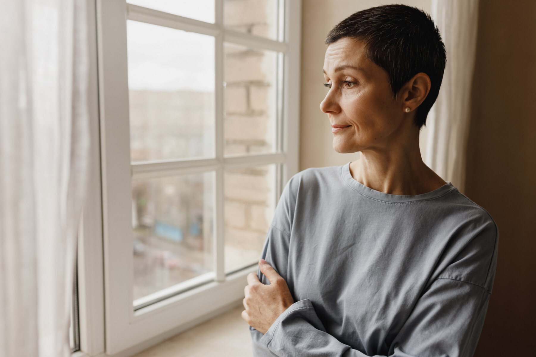 A woman with a pensive expression looks out a window.