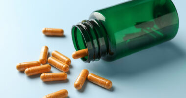 An image of capsules and an overturned bottle on a light blue background.