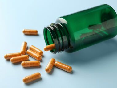 An image of capsules and an overturned bottle on a light blue background.