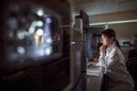 A person in a lab coat views a monitor in a laboratory,