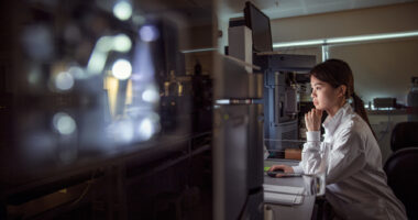 A person in a lab coat views a monitor in a laboratory,
