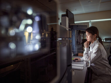 A person in a lab coat views a monitor in a laboratory,