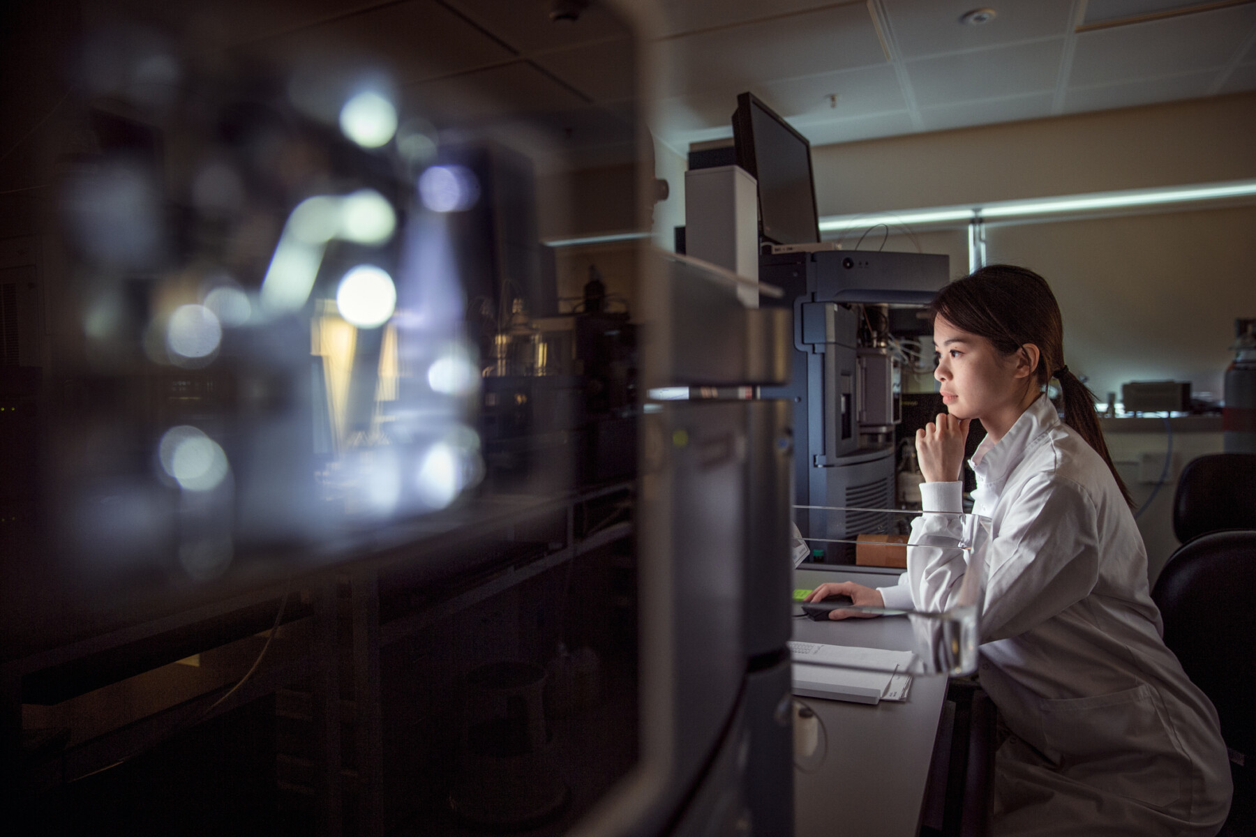 A person in a lab coat views a monitor in a laboratory,