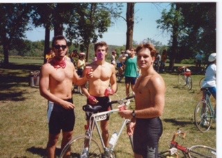 A photo with a cool retro-looking filter shows three shirtless young men standing in a park area with trees, surrounded by bicycles, and it appears they're drinking cans of beer or soda. 
