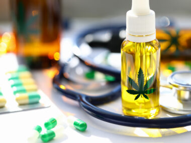 A bottle of cannabis oil stands next to a stethoscope and a packet of capsules.