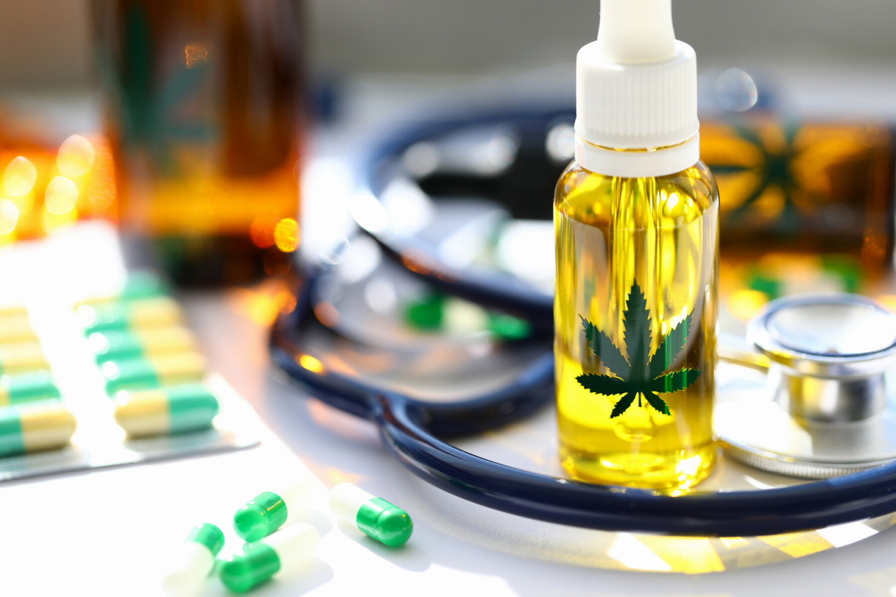 A bottle of cannabis oil stands next to a stethoscope and a packet of capsules.