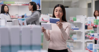 A person examines a box of medication in a drugstore.