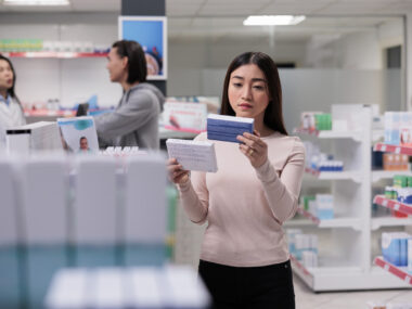 A person examines a box of medication in a drugstore.