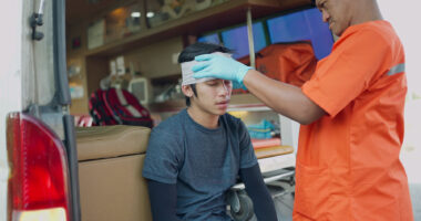 A medical professional wraps a bandage around the head of a young person who sustained an apparent head injury.