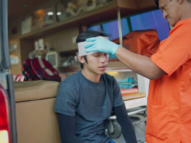A medical professional wraps a bandage around the head of a young person who sustained an apparent head injury.