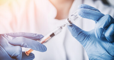 A healthcare professional wearing blue gloves draws medication from a vial into a syringe.