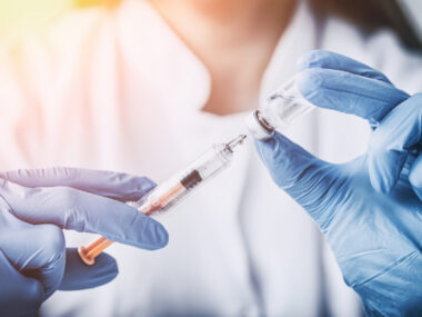 A healthcare professional wearing blue gloves draws medication from a vial into a syringe.