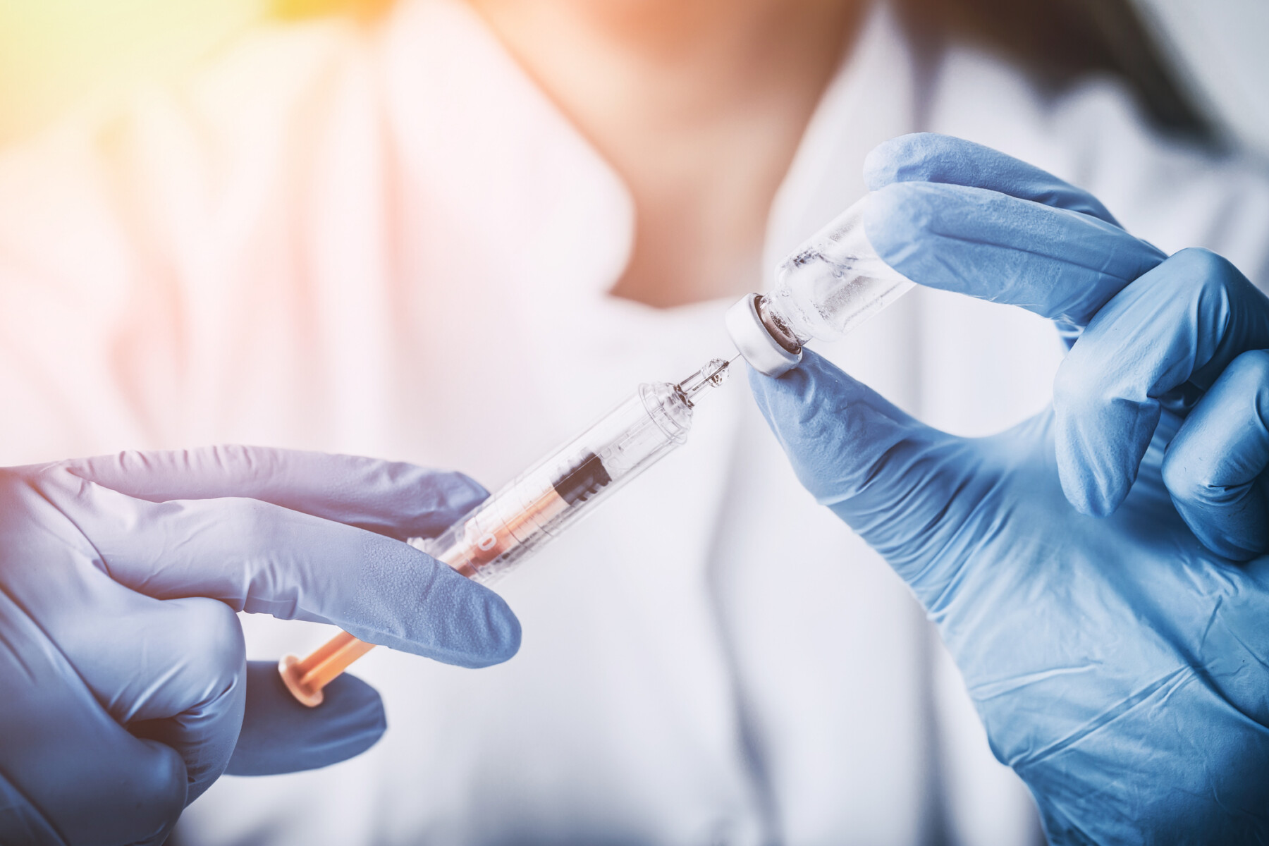 A healthcare professional wearing blue gloves draws medication from a vial into a syringe.