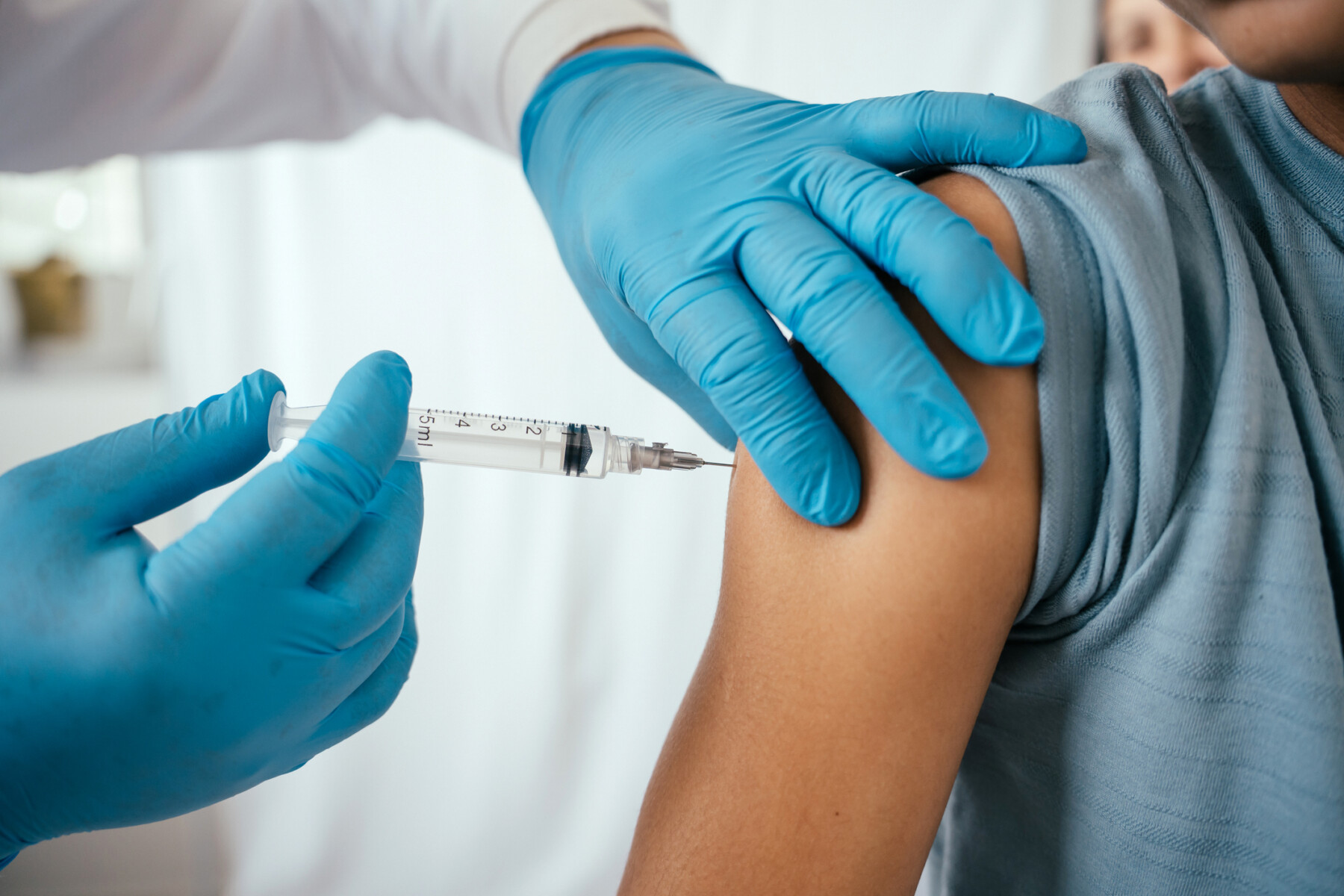 A close-up image shows gloved hands injecting a vaccination needle into a person's upper arm.