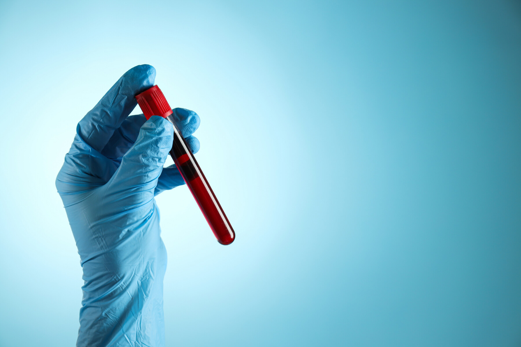 A blue-gloved hand holds a test tube filled with blood.