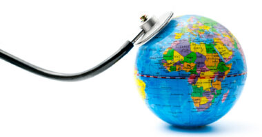 The chestpiece of a stethoscope rests on a miniature globe of the world.