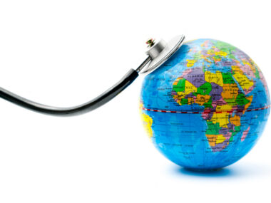 The chestpiece of a stethoscope rests on a miniature globe of the world.