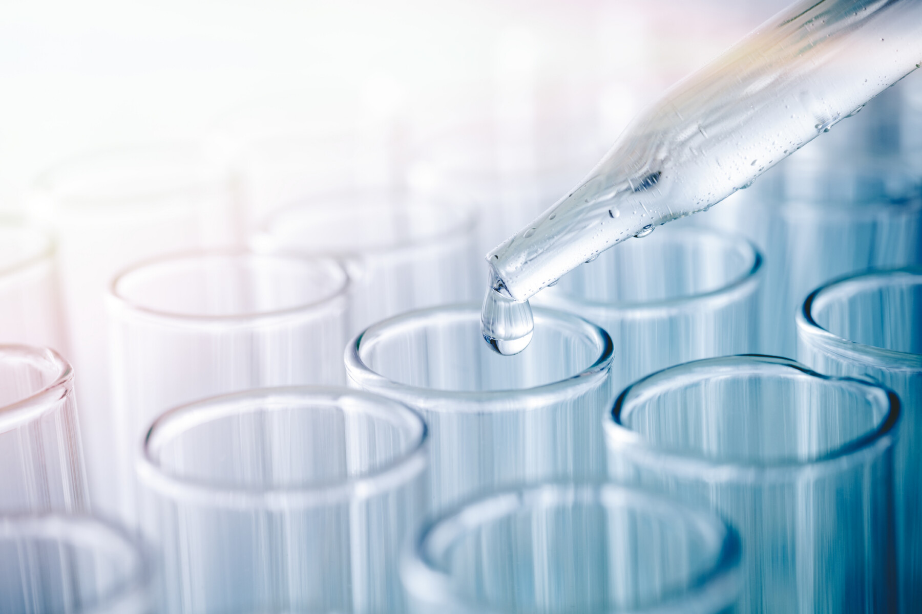 Close-up of a pipette dropping clear liquid into glass test tubes.