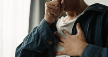 A man struggles to breathe, with one hand over his mouth and the other on his chest.