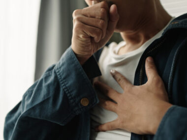 A man struggles to breathe, with one hand over his mouth and the other on his chest.