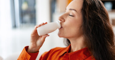 A woman drinks from a small bottle of yogurt.