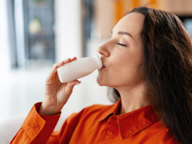 A woman drinks from a small bottle of yogurt.