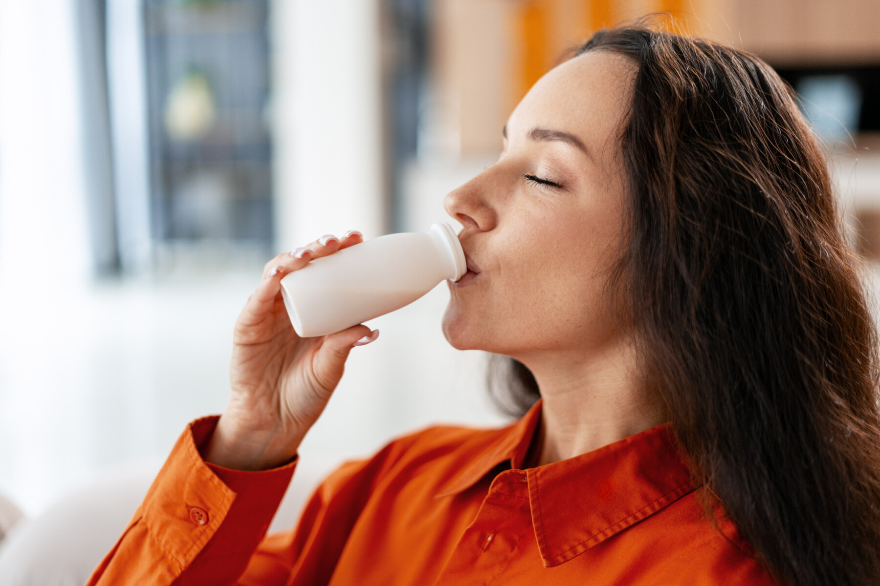 A woman drinks from a small bottle of yogurt.