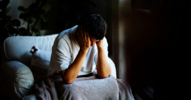 A man sits in a dark room with his head in his hands.