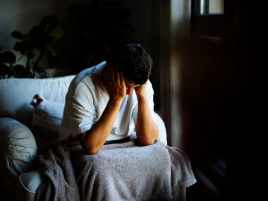 A man sits in a dark room with his head in his hands.