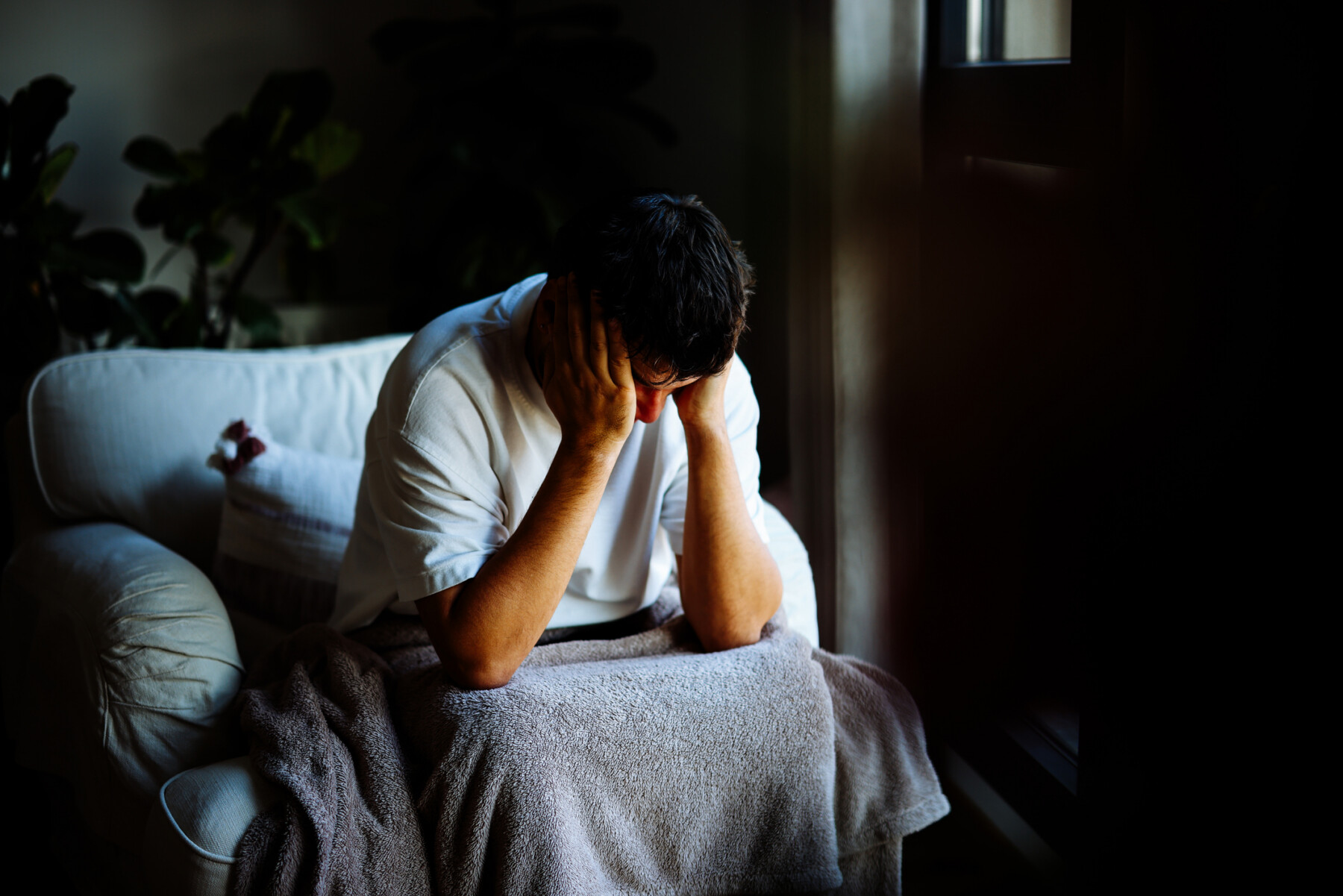 A man sits in a dark room with his head in his hands.