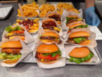 Freshly made cheeseburgers and fries are lined up in individual wrappers in a restaurant kitchen.