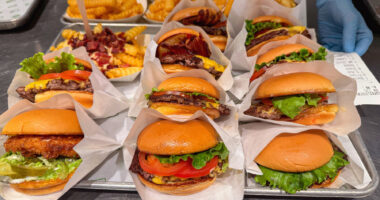 Freshly made cheeseburgers and fries are lined up in individual wrappers in a restaurant kitchen.