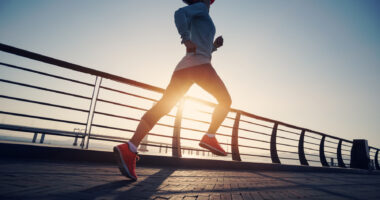 A woman running outdoors along a waterfront path in sunlight.
