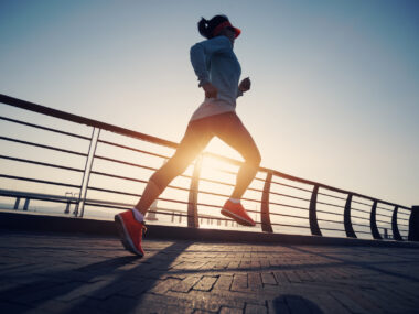 A woman running outdoors along a waterfront path in sunlight.