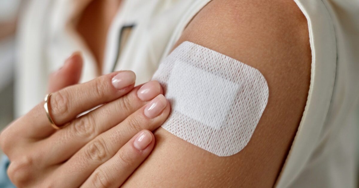 In a close-up image, a person applies a skin patch to the upper arm