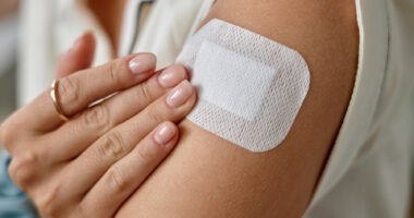 In a close-up image, a person applies a skin patch to the upper arm.