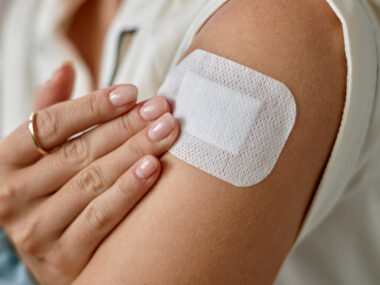 In a close-up image, a person applies a skin patch to the upper arm.