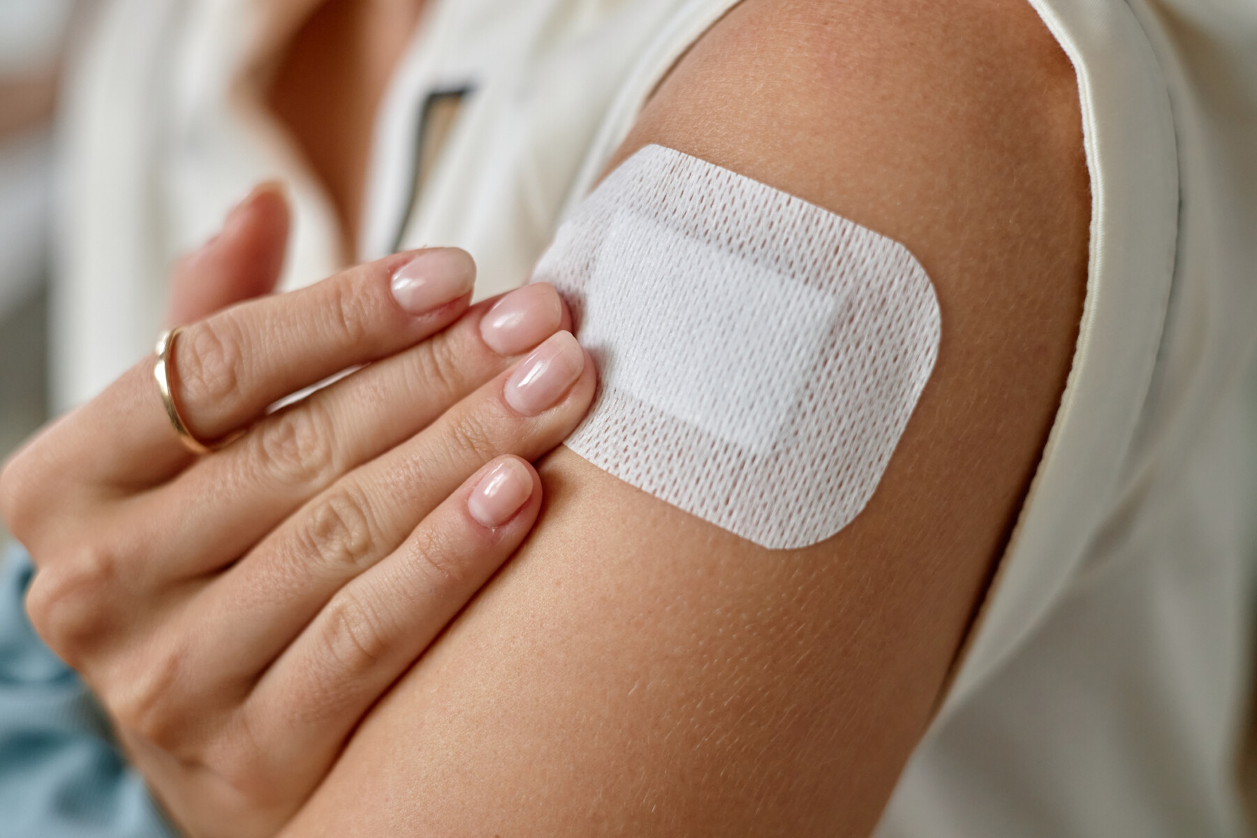 In a close-up image, a person applies a skin patch to the upper arm.