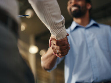 A person in a white coat shakes hands with a smiling man wearing a blue shirt.