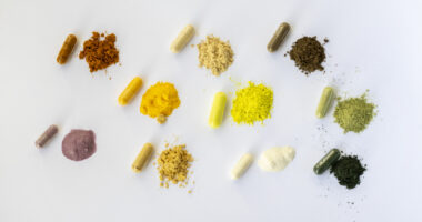 Assorted colorful capsules and small piles of powdered supplements arranged in rows on a white background.