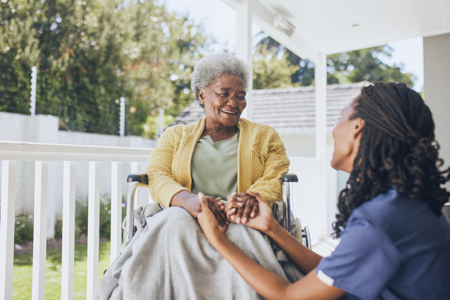 A young female nurse holds the hands of an older patient in a wheelchair.