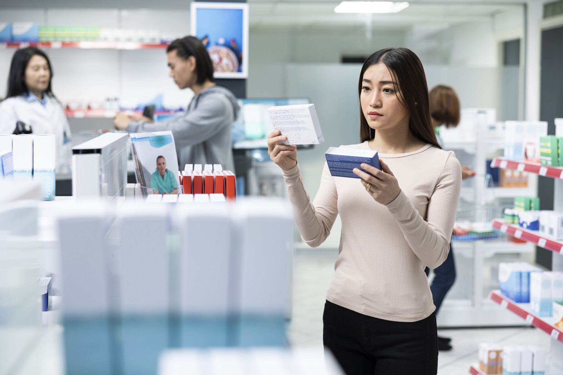 A woman holds a medication package in each hand, comparing them, while visiting a pharmacy.