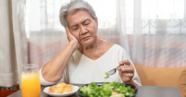 A woman rests her head on her hand with eyes closed as she eats a salad.
